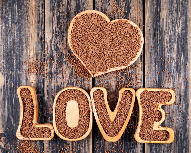 Some buckwheats on heart shape and love word on dark wooden background, top view.