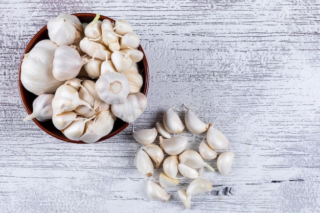 Some bunches of garlic in a bowl and nearby on light wooden table, top view.