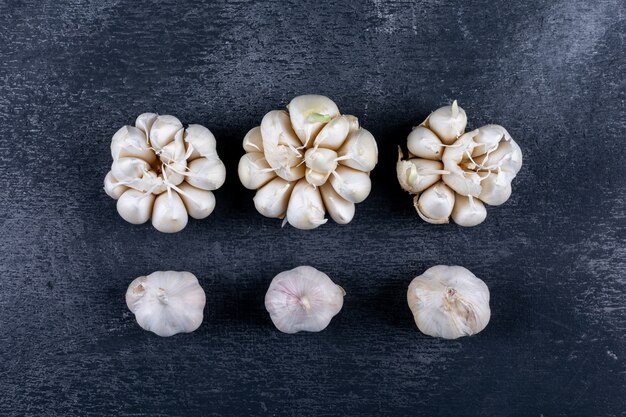 Some bunches of garlic lined up on dark textured table, flat lay.