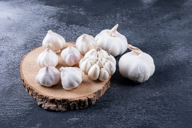 Some bunches of garlic on a wood stub and nearby on dark textured table