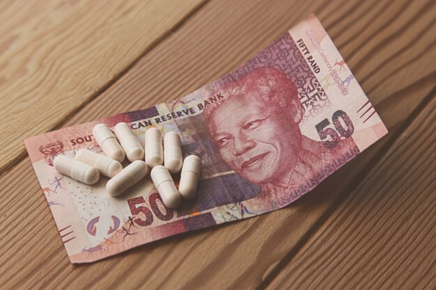 some capsules on a South African 50 rand on a wooden table