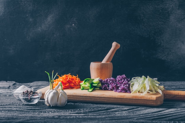 Some chopped cabbage with other vegetables in a cutting board on dark wooden background, side view.