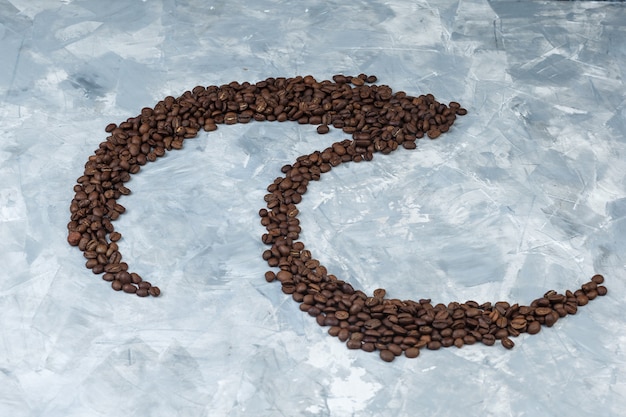 Some coffee beans on grey plaster background, high angle view.