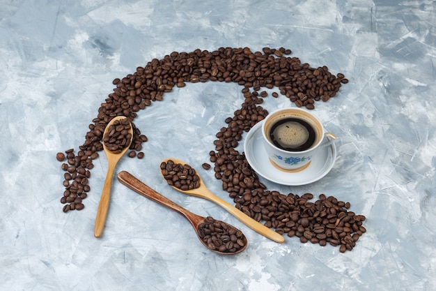 Some coffee beans with coffee drink in cup and wooden spoons on grey plaster background, flat lay.