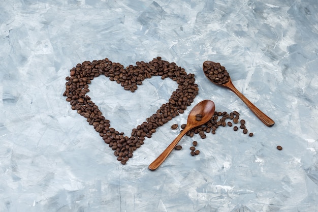 Some coffee beans in wooden spoons on grey plaster background, flat lay.