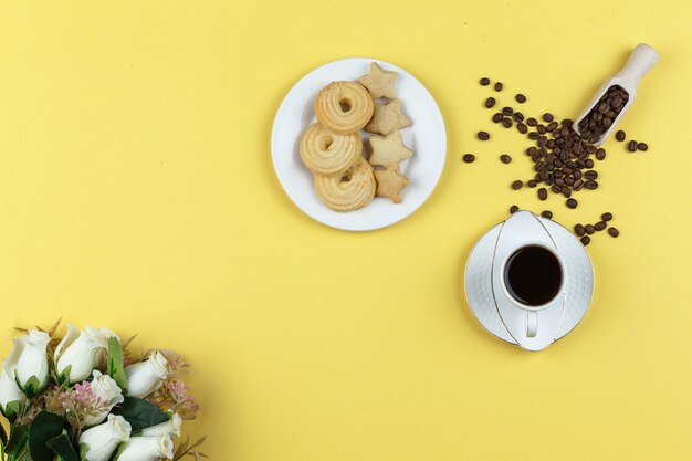 Some coffee with coffee beans and biscuits on yellow background