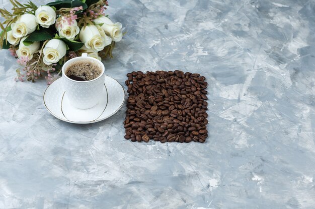 Some coffee with coffee beans, flowers in a cup on blue marble background, high angle view.