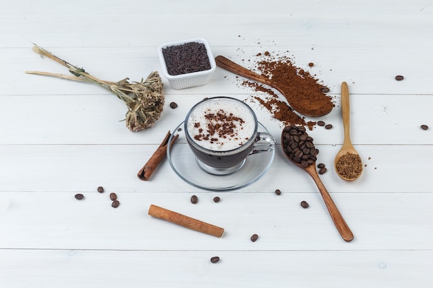 Кофе с молотым кофе, кофейные зерна, палочки корицы, сушеные травы в чашке.