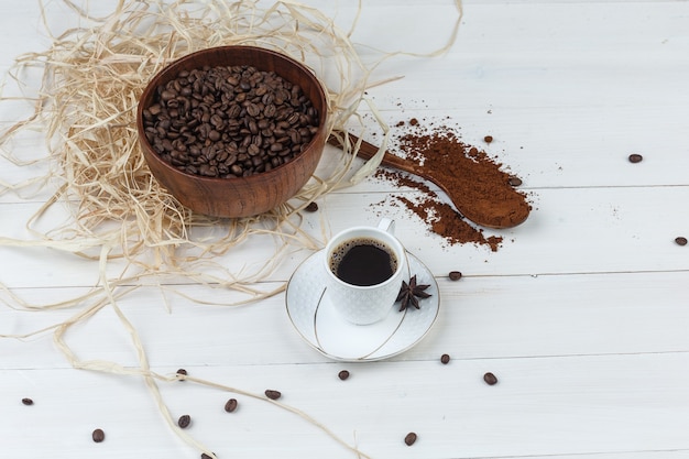 Some coffee with grinded coffee, coffee beans, spices in a cup on wooden background, high angle view.