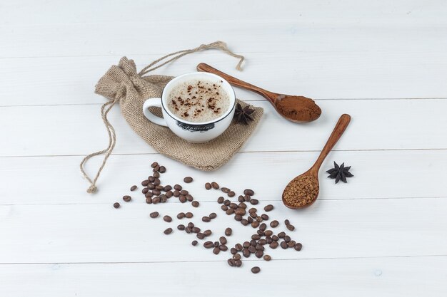 Немного кофе с молотым кофе, специями, кофейными зернами в чашке на фоне деревянных и мешков, высокий угол обзора.