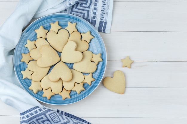 Some cookies in a plate on wooden and kitchen towel background, top view.