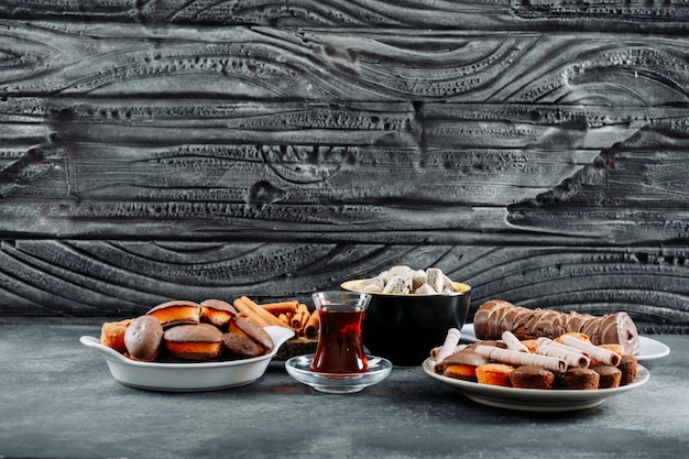 Free photo some cookies with roulade, waffles in a plates and bowl on dark wooden