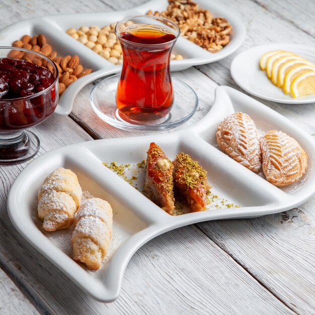 Некоторые вкусные десерты с чаем, орехами, фруктовым джемом, нарезанный лимон на белом фоне деревянные, высокий угол обзора.