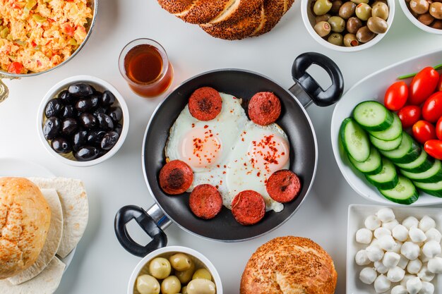 Some delicious meals with salad, pickles, turkish bagel, a cup of tea in a pan and pot on white surface, top view