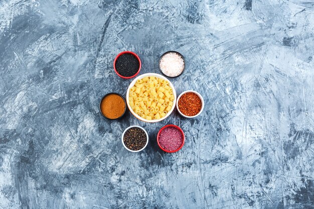 Some ditalini pasta with spices in a bowl on grey plaster background, top view.
