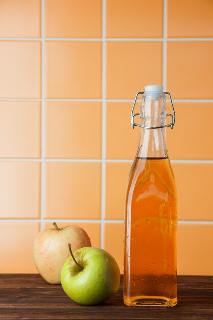 Some fresh apples with apple juice in a basket on orange tile background, side view. space for text