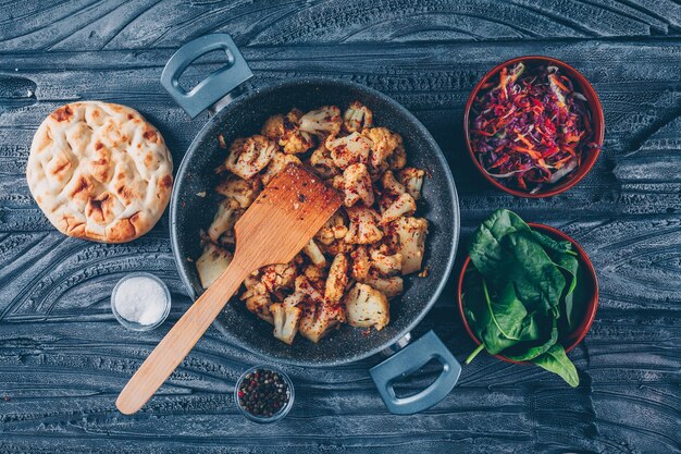 Some fried cauliflower with vegetable salad, green in a pot on dark wooden background, top view.