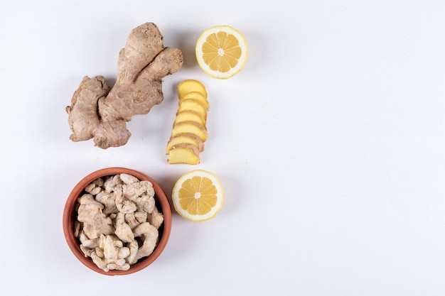 Some ginger in a bowl with slices nearby and lemon on white background, top view. space for text