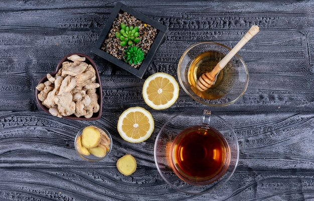 Some ginger and honey in a bowls with ginger slices, lemon on dark wooden background, top view.