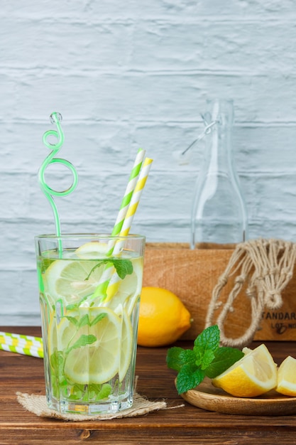 Some glass of lemon juice with wooden crate and rope on wooden and white surface, side view. copy space for text