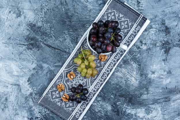 Some grapes with walnuts in a white cup on grunge and kitchen towel background, top view.