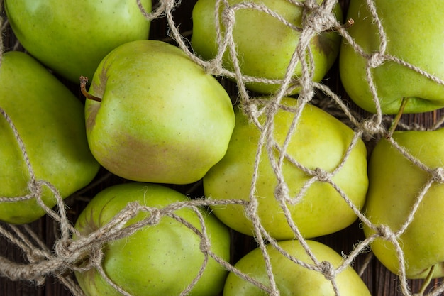 Free photo some green apples in a net bag on wooden background, top view.