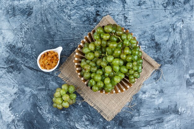 Some green grapes with raisins in a basket on grunge and piece of sack background, flat lay.