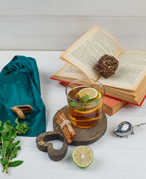 Un po 'di tisana e cannella con libri, limone, spezie e sciarpa verde su una tavola di legno