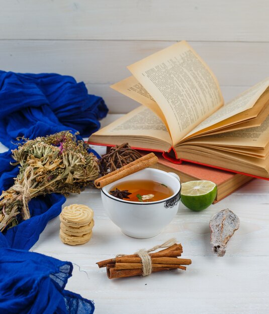 Травяной чай, печенье и цветы с книгами, лимоном, специями и синим шарфом.