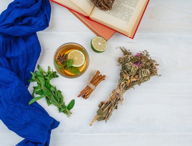 Some herbal tea and flowers with books, lemon, spices and blue scarf on white surface