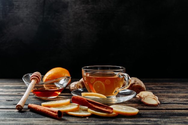 Some lemon with ginger, honey, dry cinnamon, tea on dark wooden and black background, side view. space for text