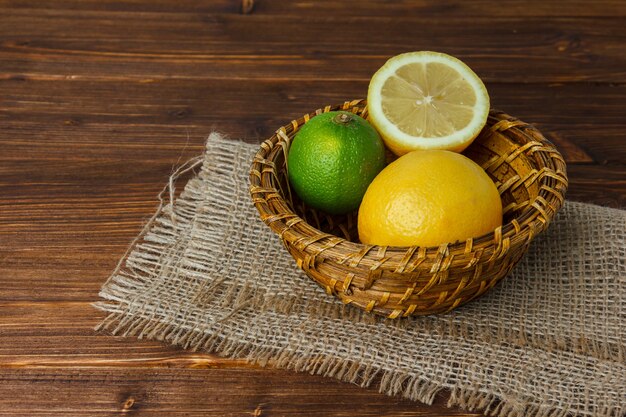 Some lemon with half of lemon on piece of sack in a basket on wooden surface, high angle view. space for text