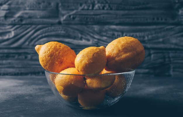 Some lemons in a glass bowl on dark wooden background, side view.