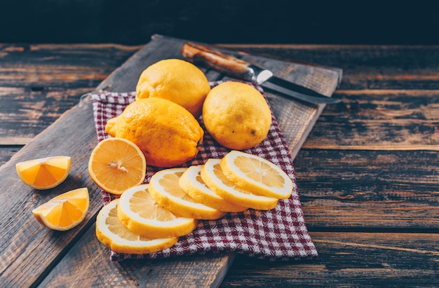 Some lemons with knife, slices on dark wooden background, high angle view.