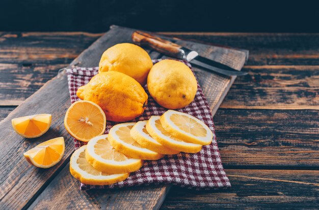 Some lemons with knife, slices on dark wooden background, high angle view.