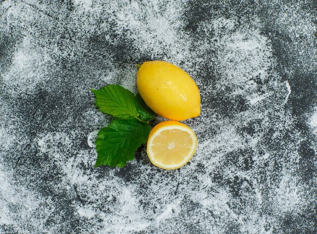 Некоторые лимоны с листьями на серой текстурированной поверхности, вид сверху.