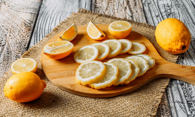 Some lemons with slices on cutting board, cloth and dark background, high angle view.