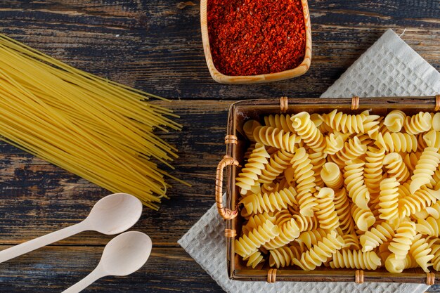 Some macaroni pasta with spaghetti, spoons in a tray on wooden background, top view.