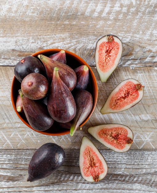 Free photo some mission figs and halves in a bowl and around on wooden table, top view.