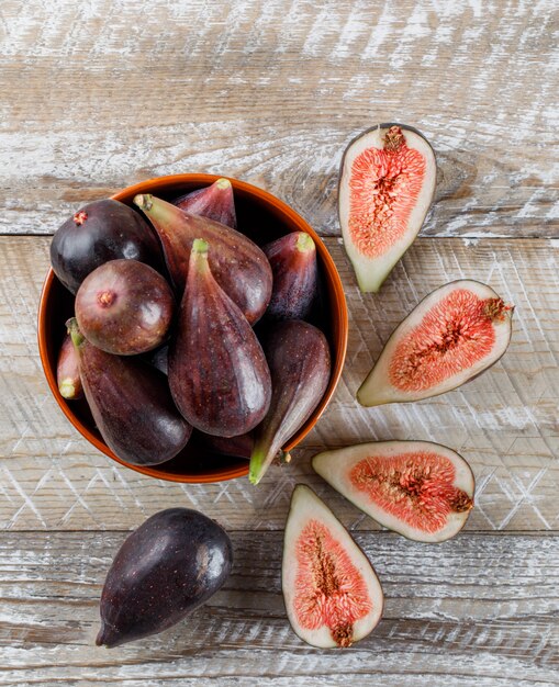 Some mission figs and halves in a bowl and around on wooden table, top view.