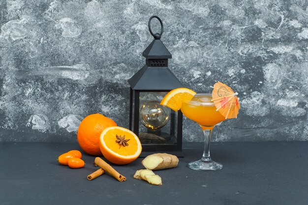 Некоторые апельсины с античный свет, сок в стакан, имбирь и кусочки на текстурированной поверхности, вид сбоку.