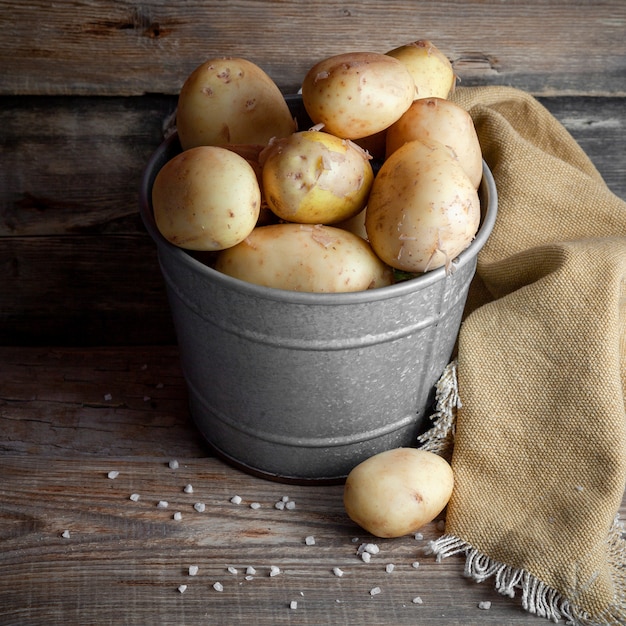 Some potatoes in a gray bucket on dark wooden background, high angle view.