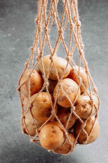 Free photo some potatoes in a net bag on dark textured background, side view.