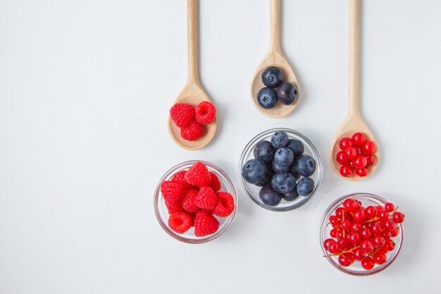 Some raspberries with blueberries in a spoons and saucers, top view.