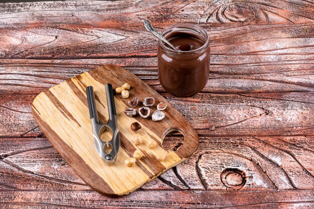 Some of shelled and cleaned hazelnuts with cocoa spread and nutcrackers on wooden table, top view.