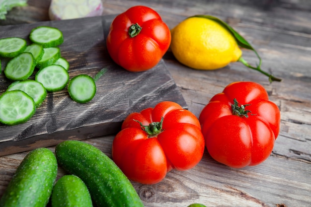 Free photo some sliced cucumber with garlic, tomatoes, lemon in a cutting board on dark wooden background, high angle view