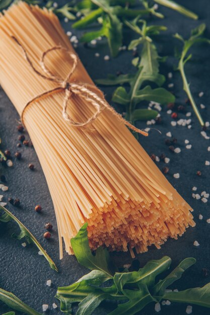 Некоторые макароны спагетти с зелеными на сером фоне текстурированных, высокий угол обзора.