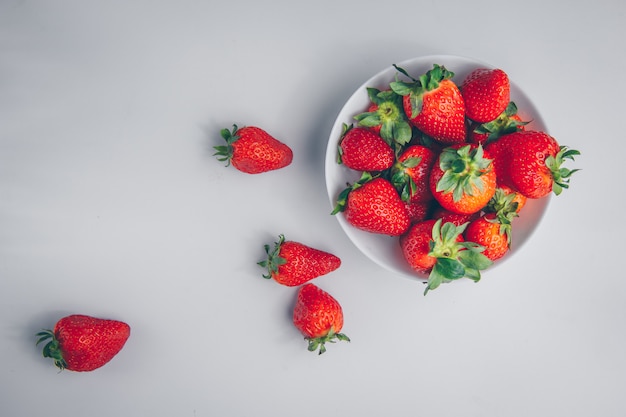 Some strawberries in a bowl on white background, top view.