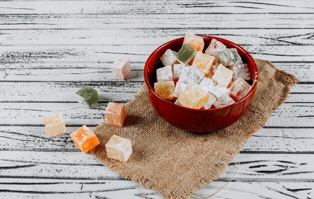 Some turkish delight lokums in a bowl on cloth and white wooden background, high angle view.