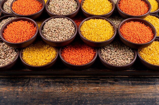 Some of yellow, green and red lentils in a brown bowls on dark wooden table, high angle view.